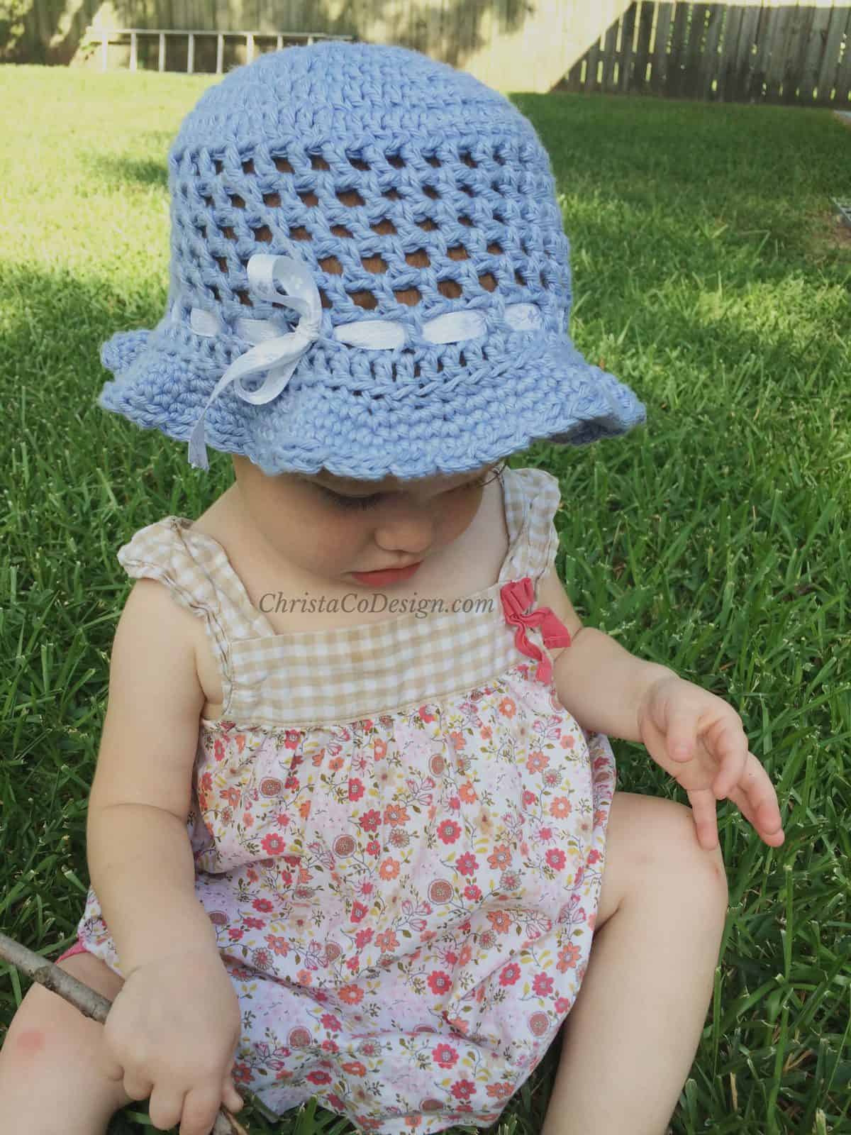 Toddler girl in blue crochet sun hat on grass.