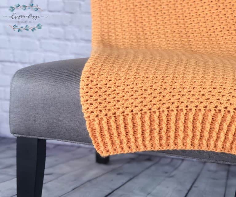 Orange crochet blanket draped on grey chair.