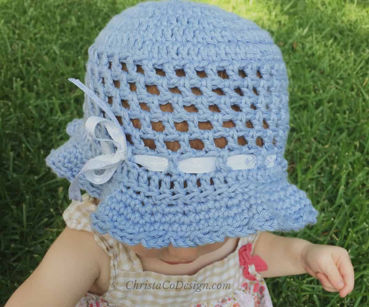 Toddler in blue sun hat with ribbon.