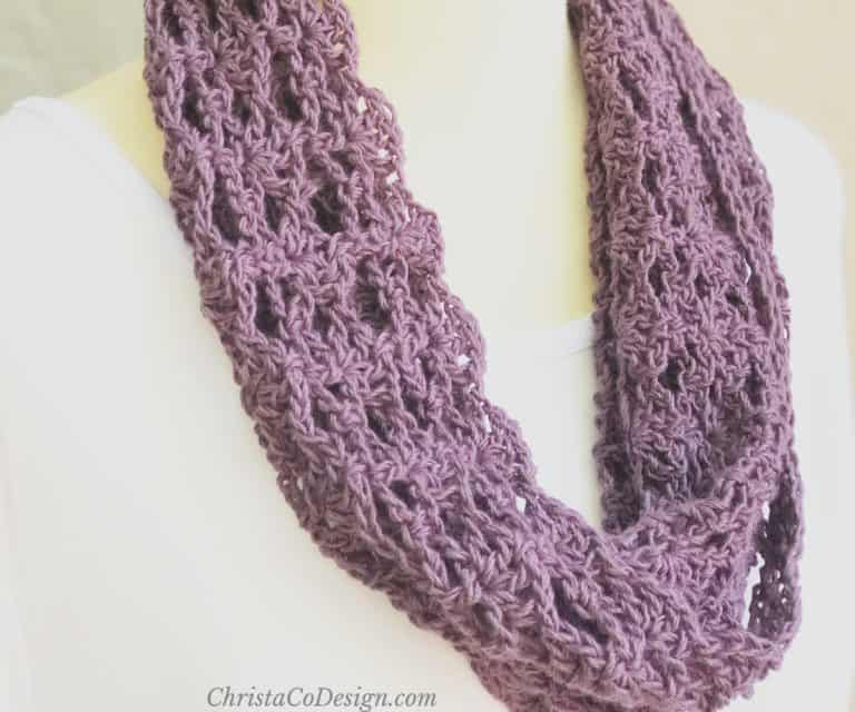 Lacy crochet cowl in purple whims merino yarn draped on mannequin.
