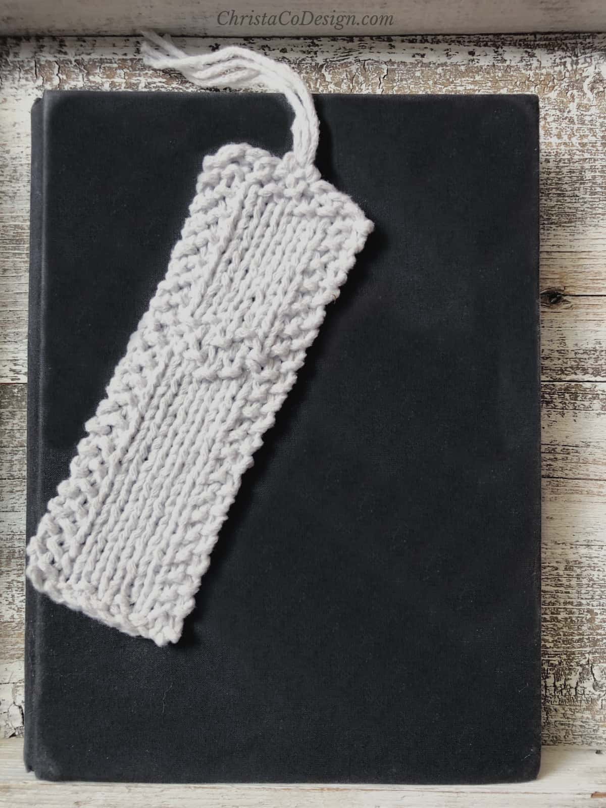 White knitted bookmark with fringe and heart detail on black book.