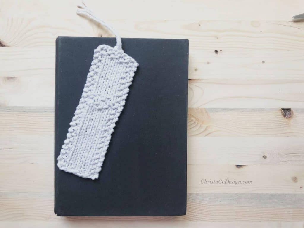 picture of beginner knit bookmark in white with heart detail on black book