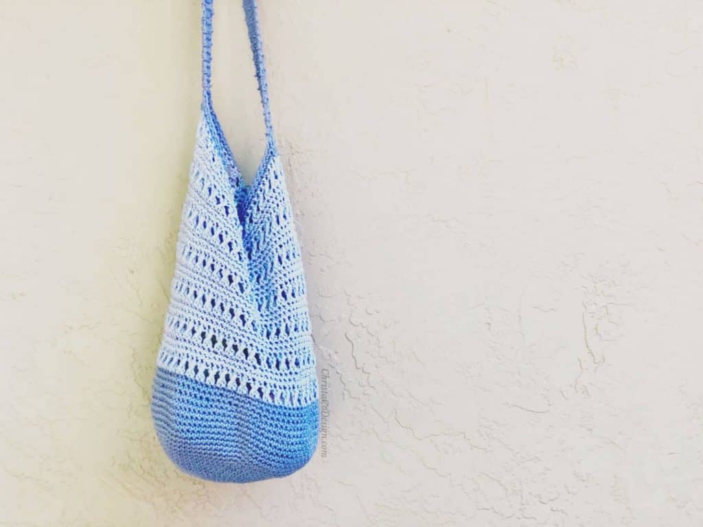 Blue crochet shoulder bag hanging against beige wall.