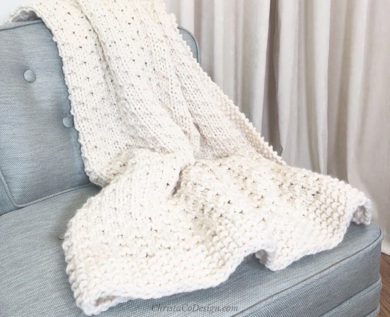 Bella vita easy knit blanket beginner knitting pattern in cream yarn on blue chair.