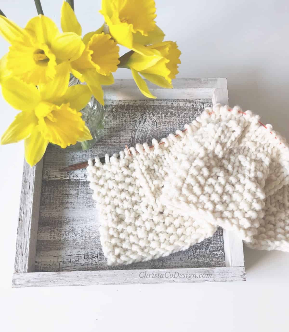 Yellow daffodils next to blanket cast on and knit for a few inches.