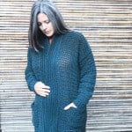 Woman wrapped in oversized cardigan with hand in pocket.