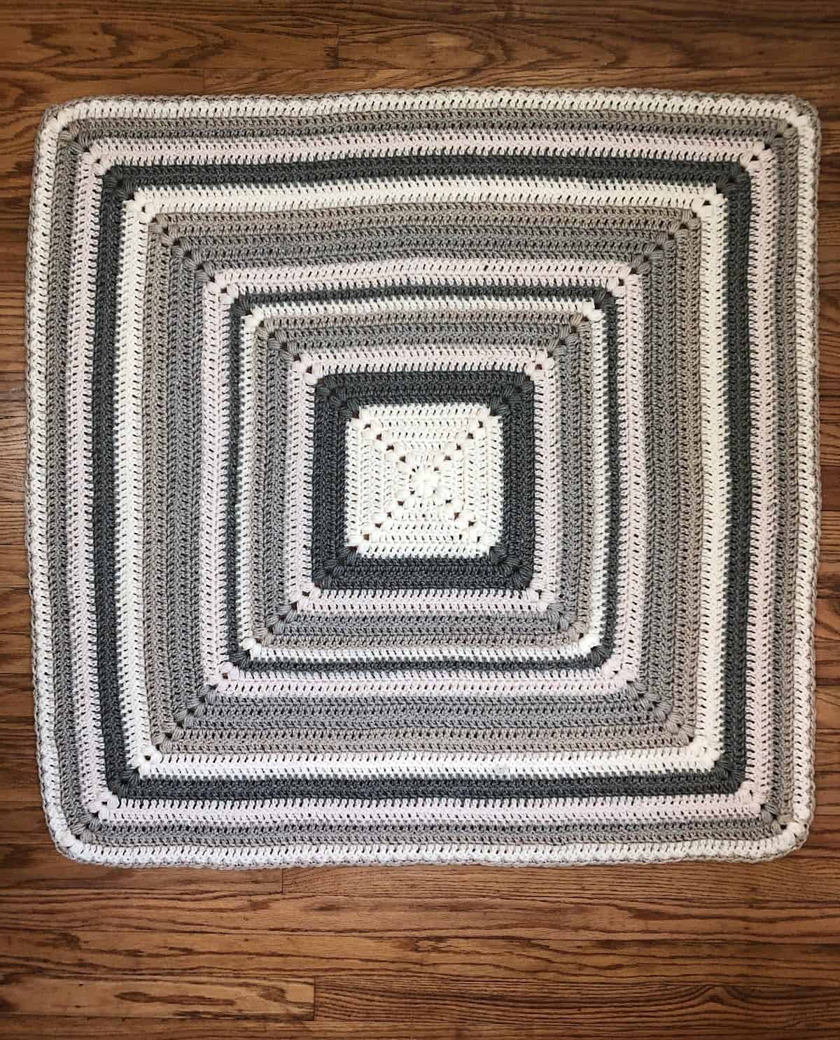 Center out crochet blanket in grey and white laid out flat on wood floor.