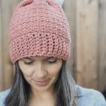 Pink bottom up hat crochet pattern with white pom on woman looking down.