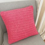 Red crochet pillow with envelope closure on grey chair.