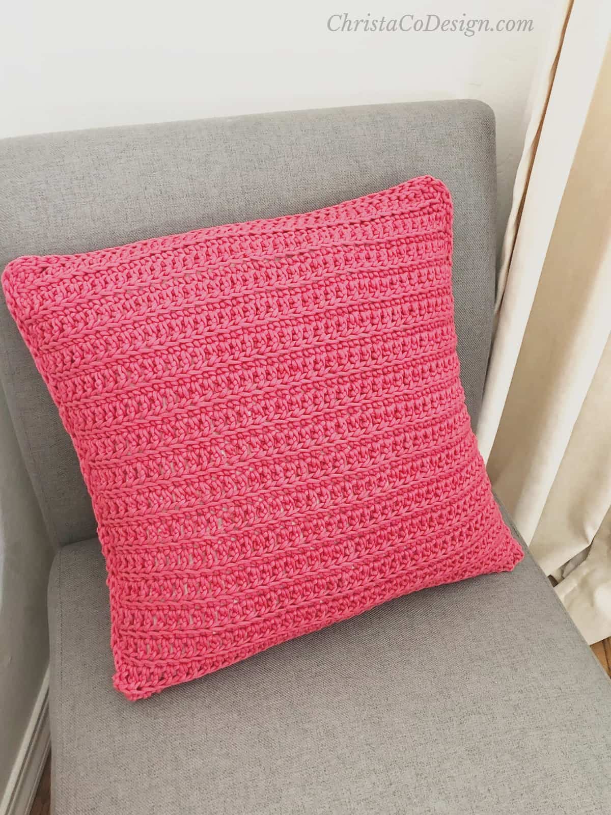Red crochet pillow with envelope closure on grey chair.