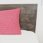 picture of red crochet pillow on wood and white bed