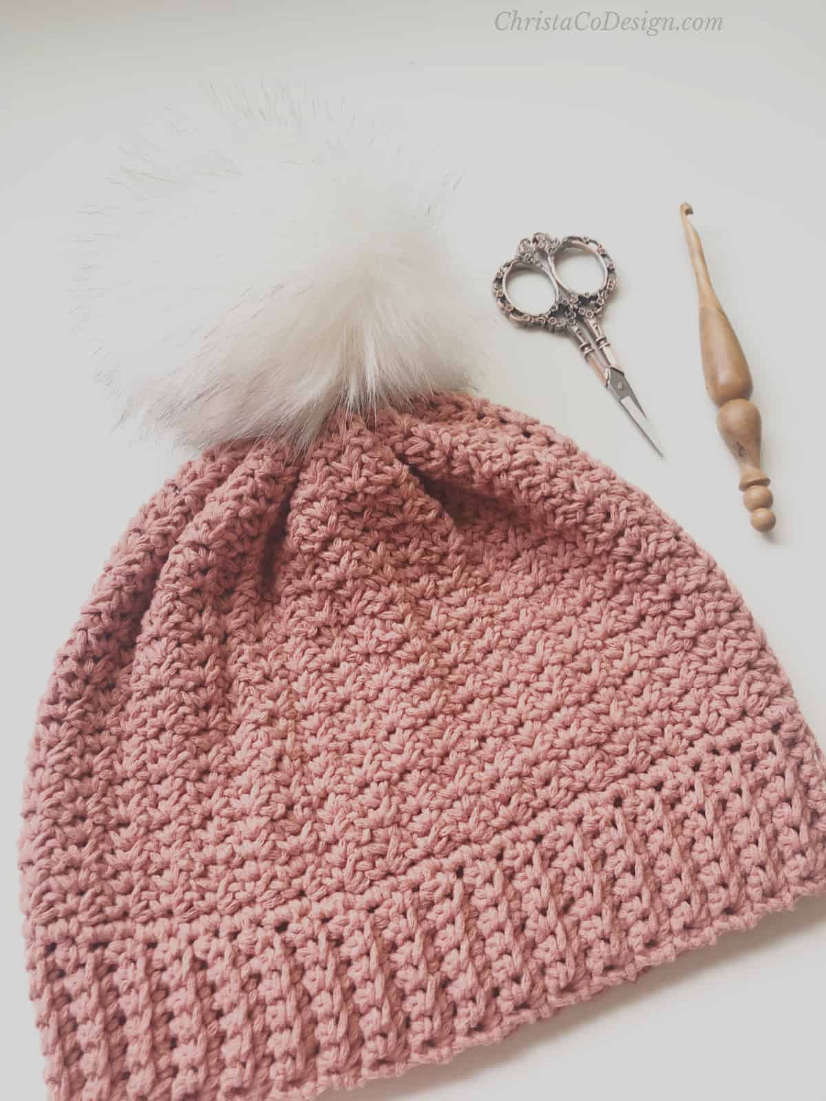 picture of pink crochet hat with ribbing flat and scissors and hook