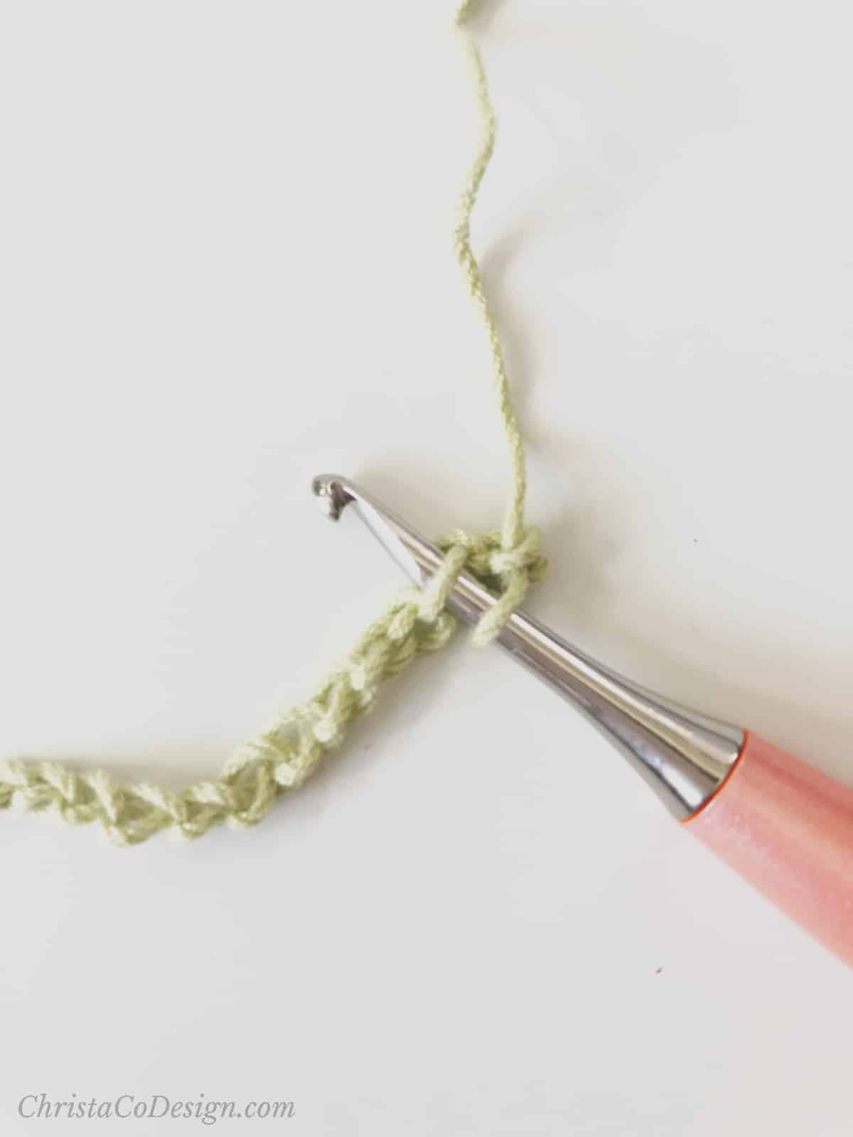 picture of peach crochet hook inserted into chain of green stitches