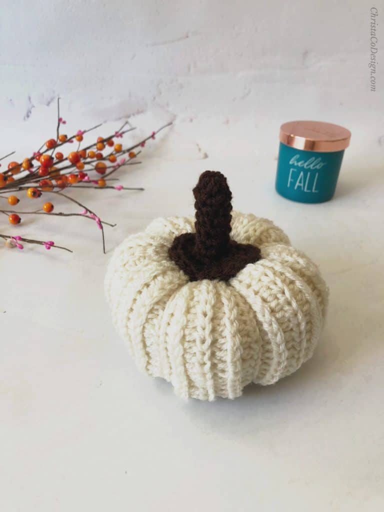 White crochet pumpkin with stem blue candle white background.