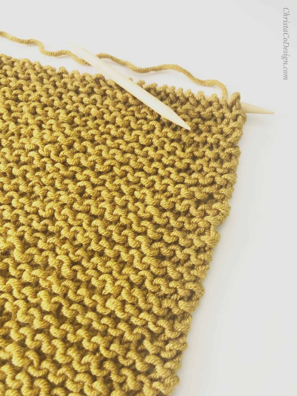 Mustard yellow garter stitch shawl on knitting needles.