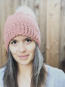 picture of woman smiling at camera in pink crochet hat with faux fur pom in white