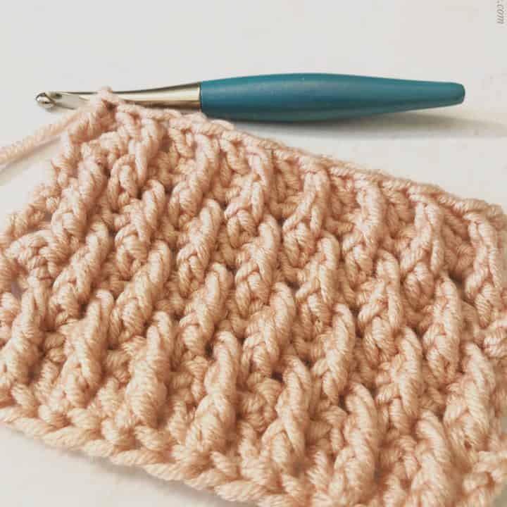 Alpine stitch swatch in pink yarn with blue hook.