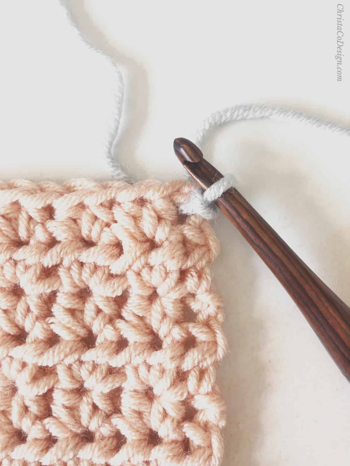 Joining grey yarn by pulling through on crochet blanket.