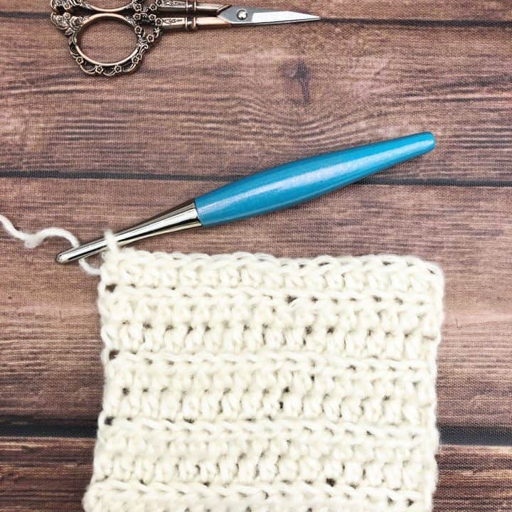 Crochet square swatch in white yarn with blue hook.