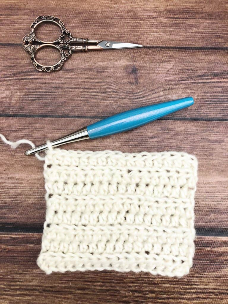 Crochet square swatch in white yarn with blue hook.