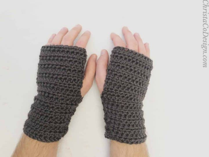 Mens hands in black fingerless crochet gloves on white table.