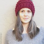 Woman in chunky maroon knit beanie with pom in grey sweater.