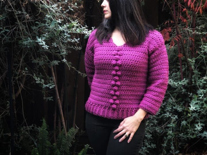A woman looks to the side while modeling the Briones Bobble Sweater Crochet Pattern in pink.
