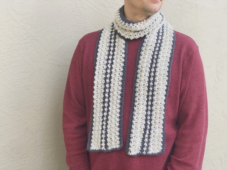 Man in burgundy sweater with striped grey and charcoal crochet scarf on.