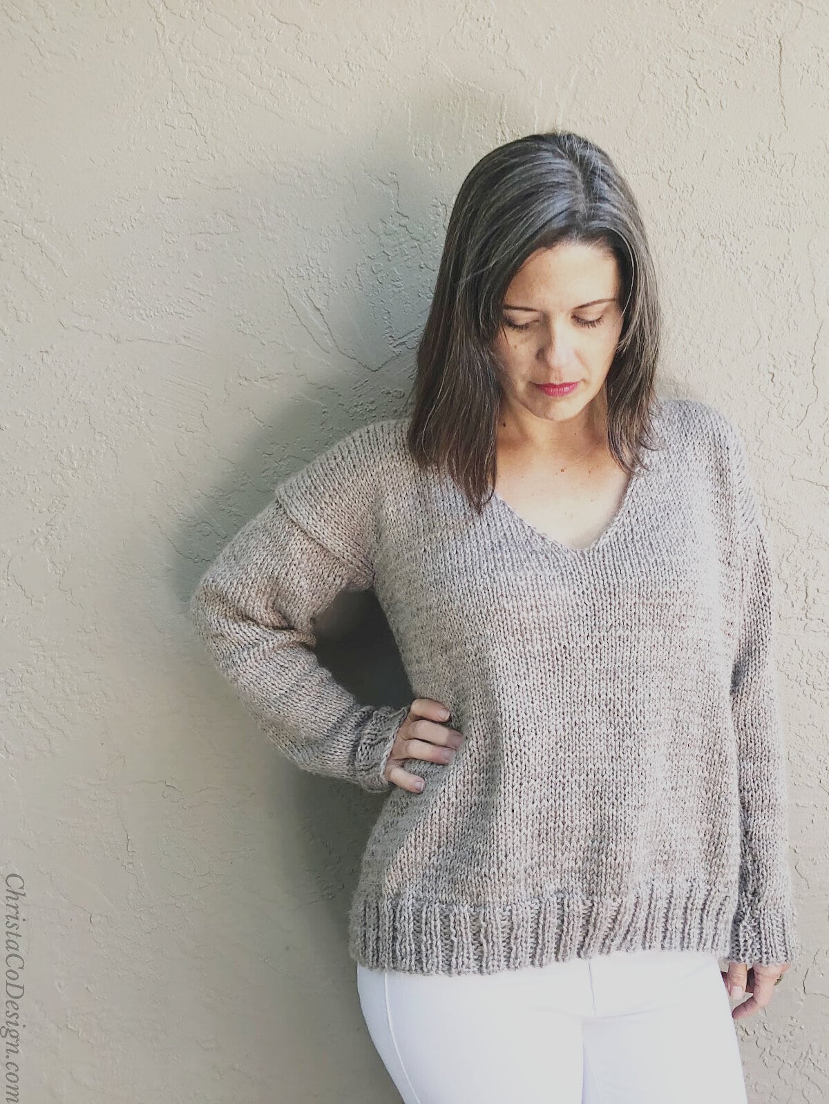 Woman looks down while wearing knit v-neck pullover.