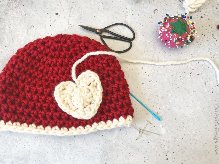 Red hat with white crochet heart and sewing supplies.