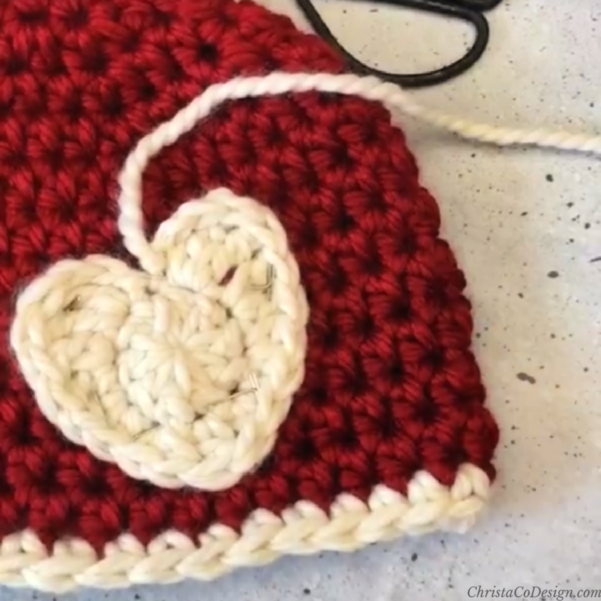 Heart applique in cream yarn on red hat.