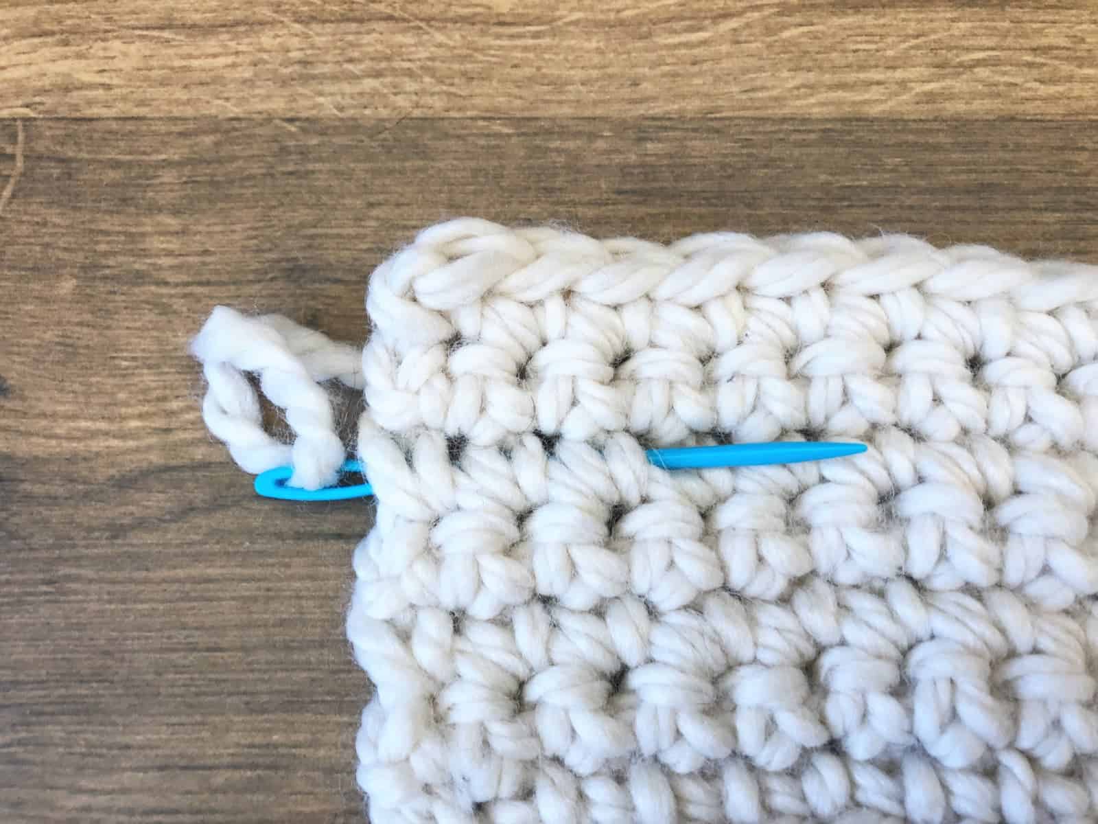 Blue needle sliding between single crochet stitches.