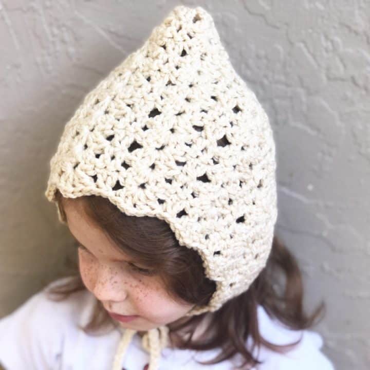 Crochet bonnet pattern in cream yarn on girl.