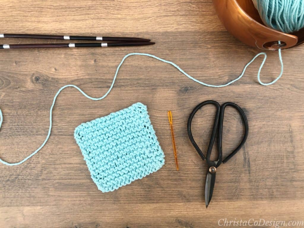 Knit scrubby pattern with needles and scissors in blue cotton yarn.