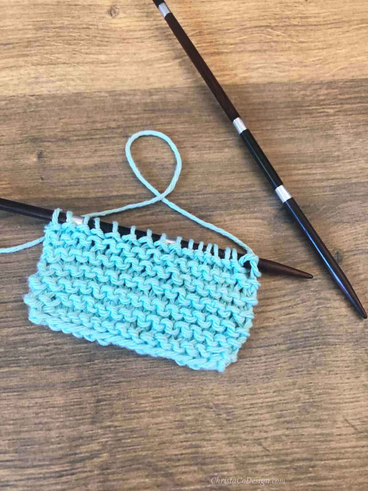 Rows of garter stitch in blue yarn on straight needle.