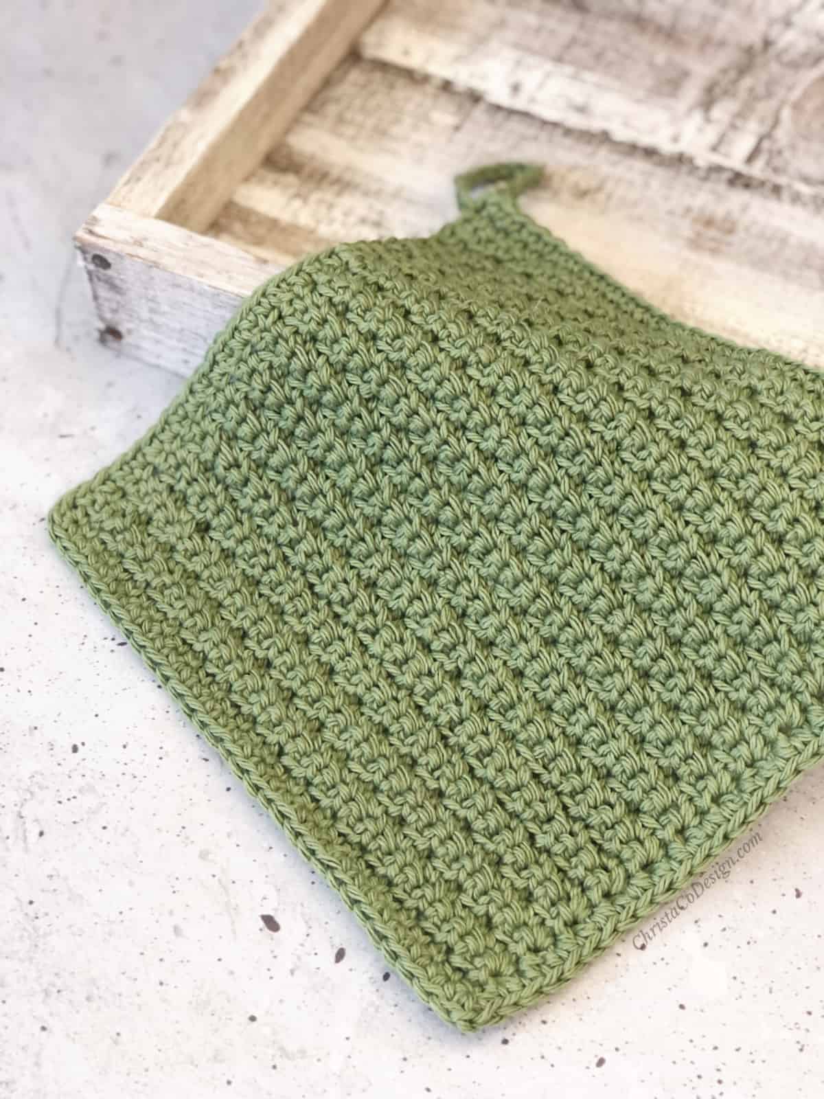 Crochet dishcloth in green on white wood block.
