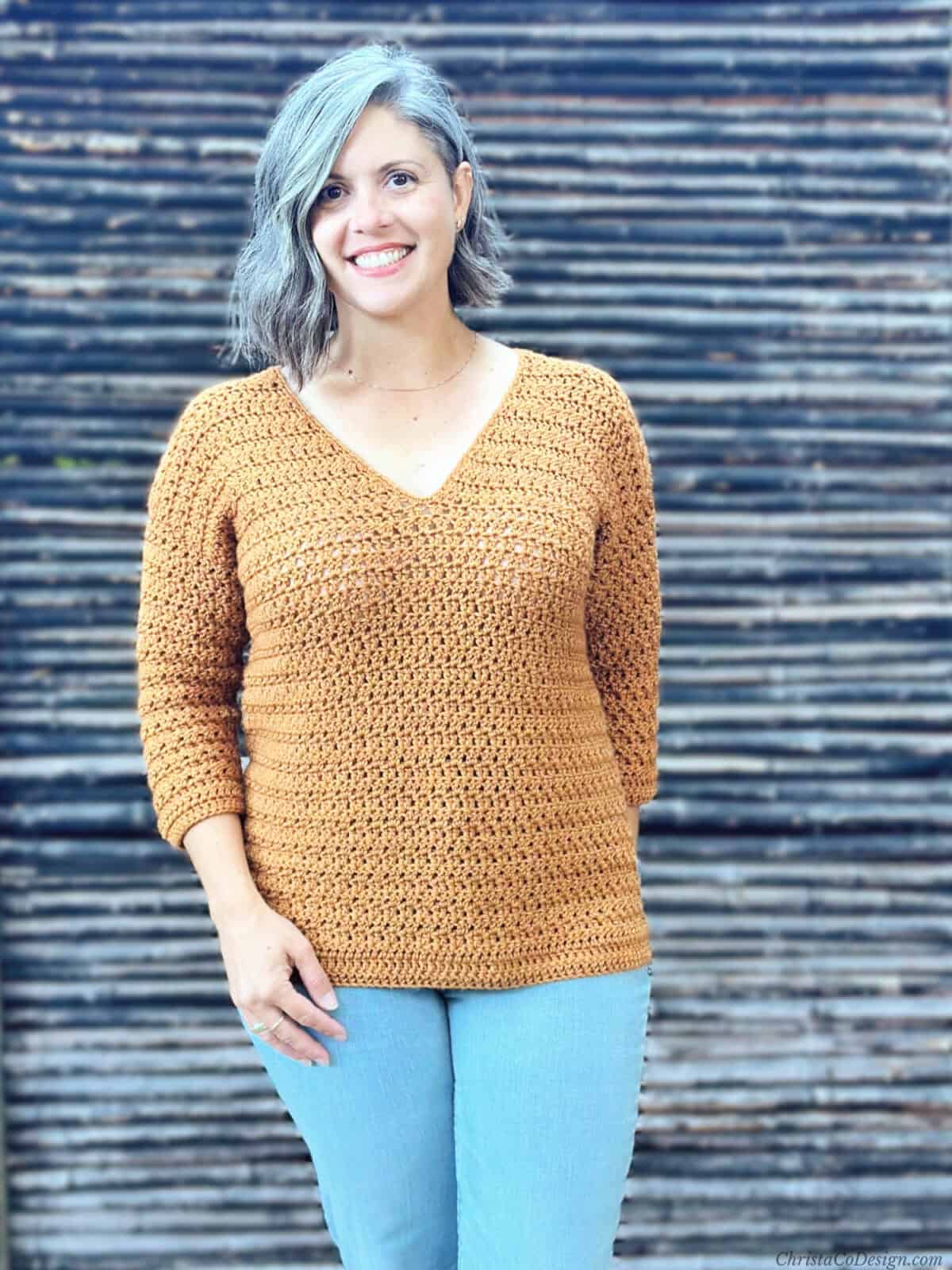 Woman smiling at camera in jeans and crochet v-neck sweater.