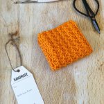Orange crochet dishcloth folded on with gift tag.