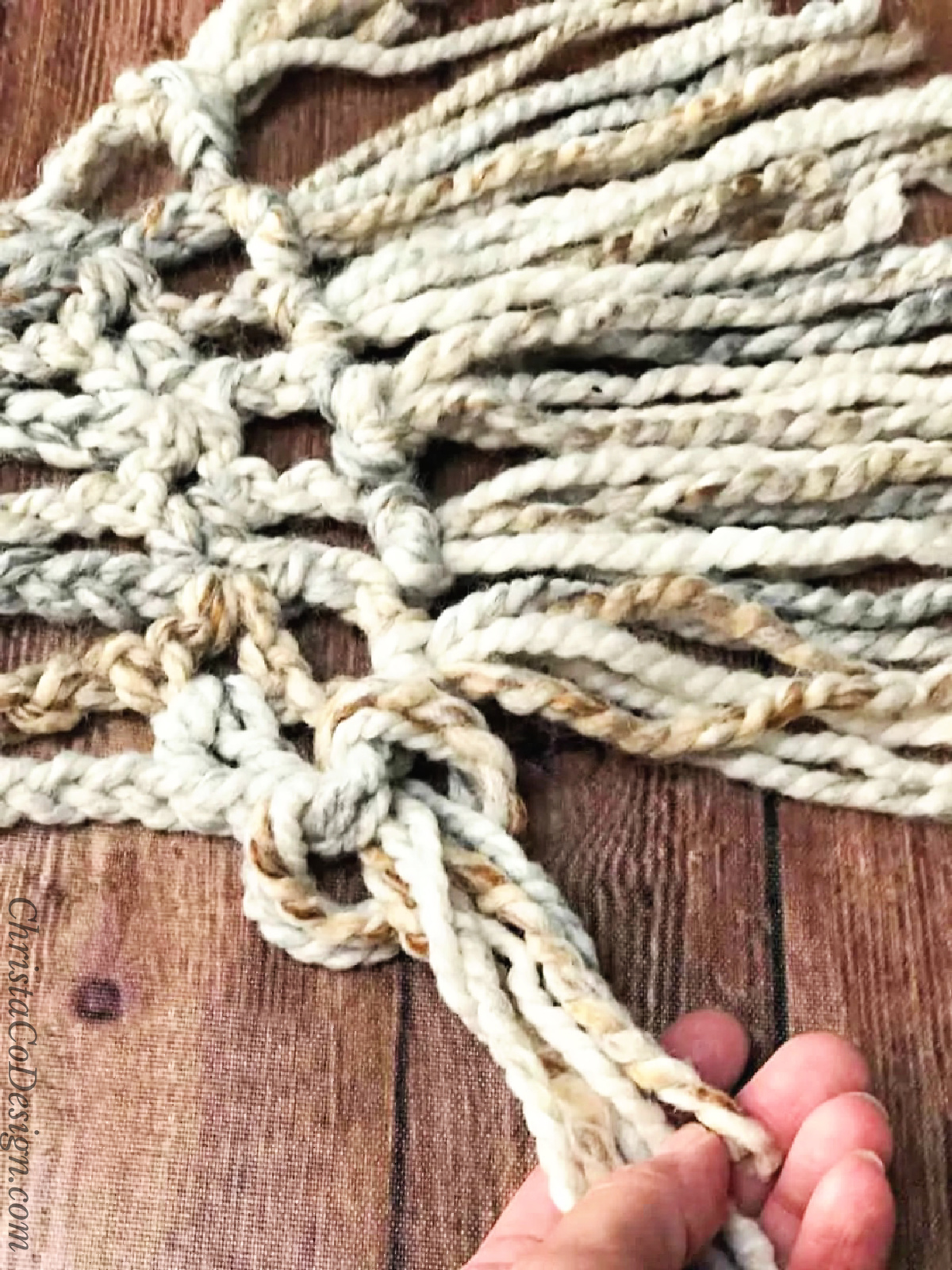 Hand pulling yarn fringe through loop.