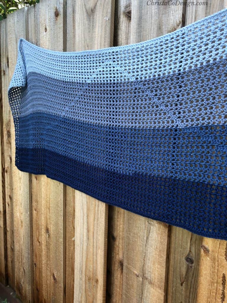 Easy rectangle crochet shawl pattern in double crochets in ombre blues on fence.
