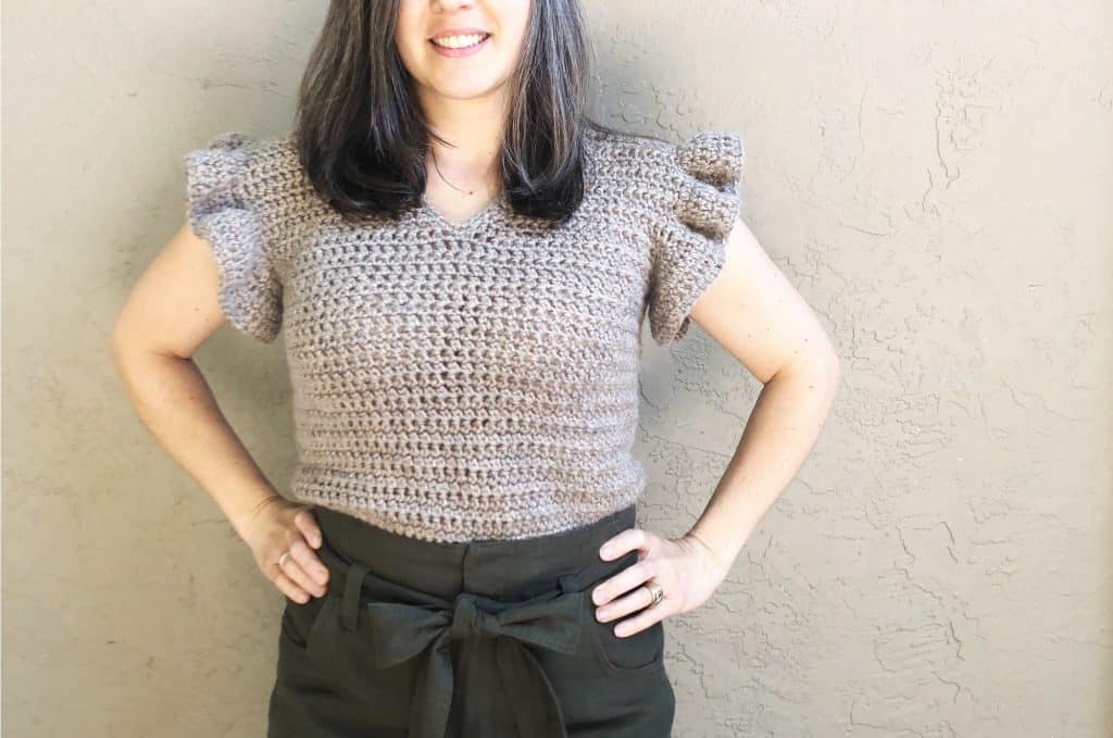 Woman in beige fitted crochet top with ruffles sleeves.