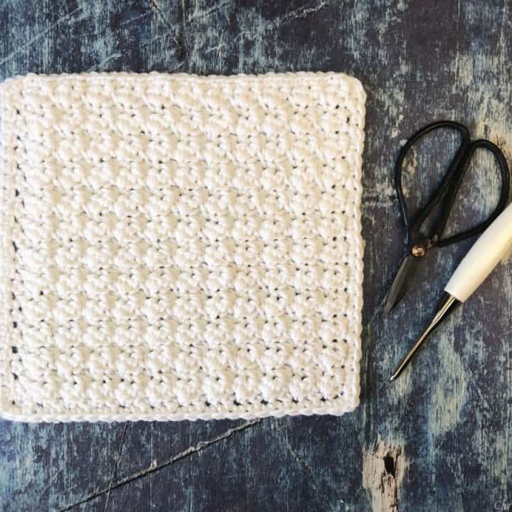 White textured crochet blanket square next to scissors and hook.