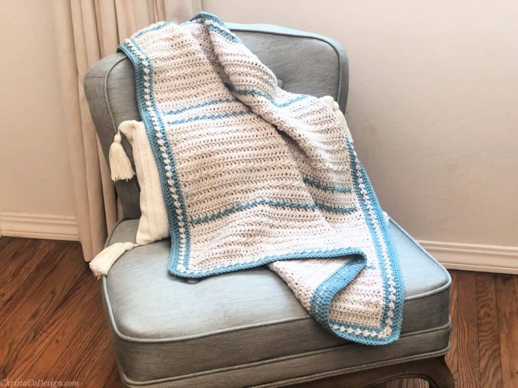 Textured crochet baby blanket on chair in cream and blue.
