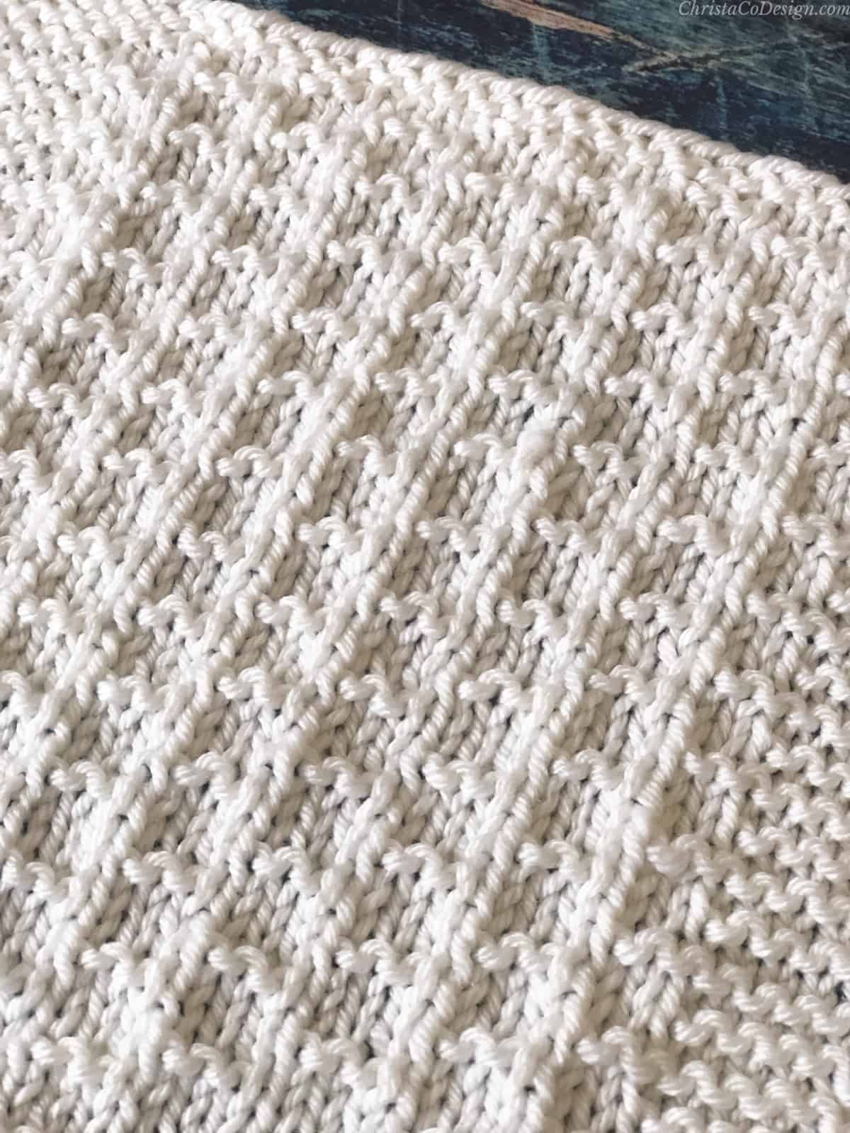 Close up textures of center on knit blanket square pattern in white.