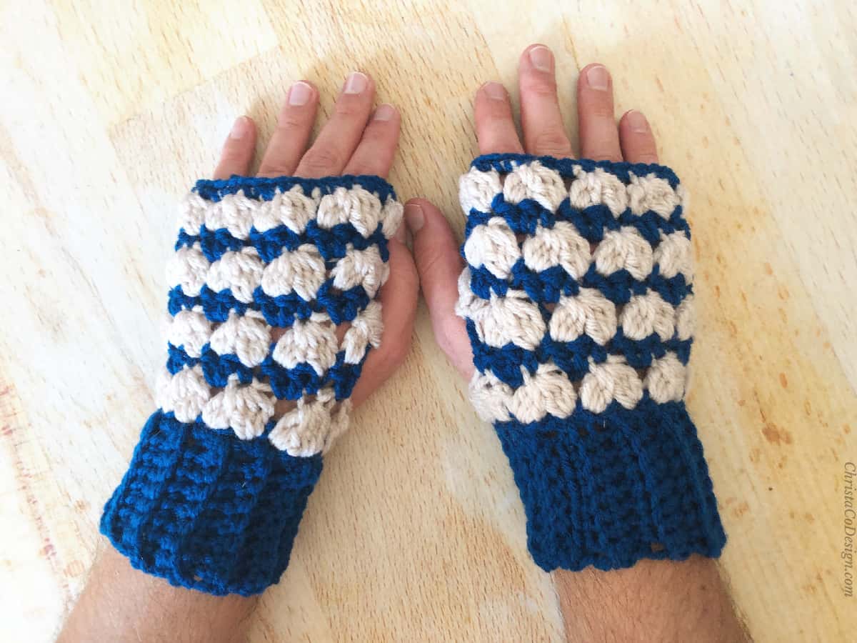 Top of man's hands in crochet gloves blue and cream textured stripes.
