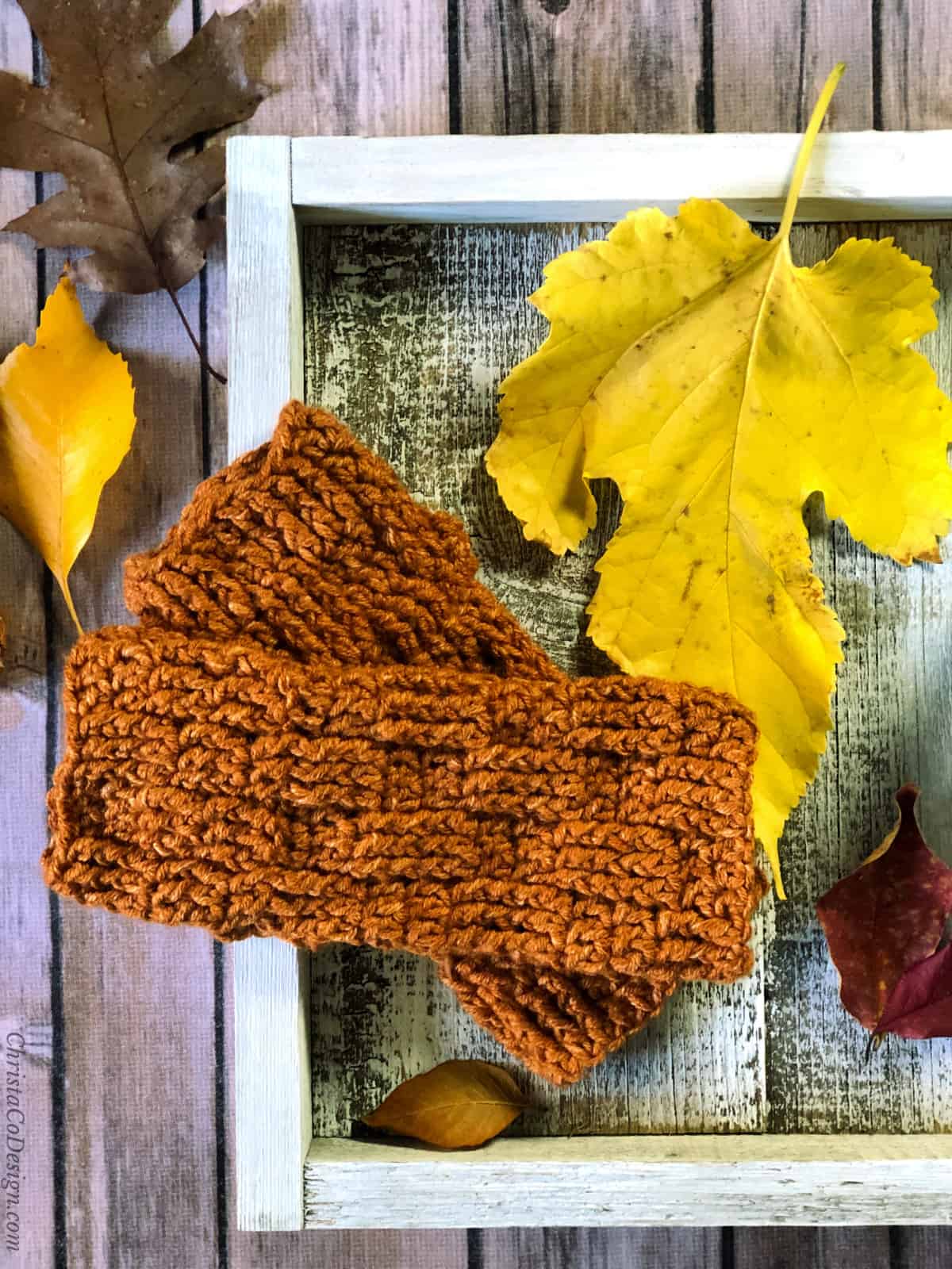 Textured fingerless gloves crochet pattern in rust yarn on white square with fall leaves.