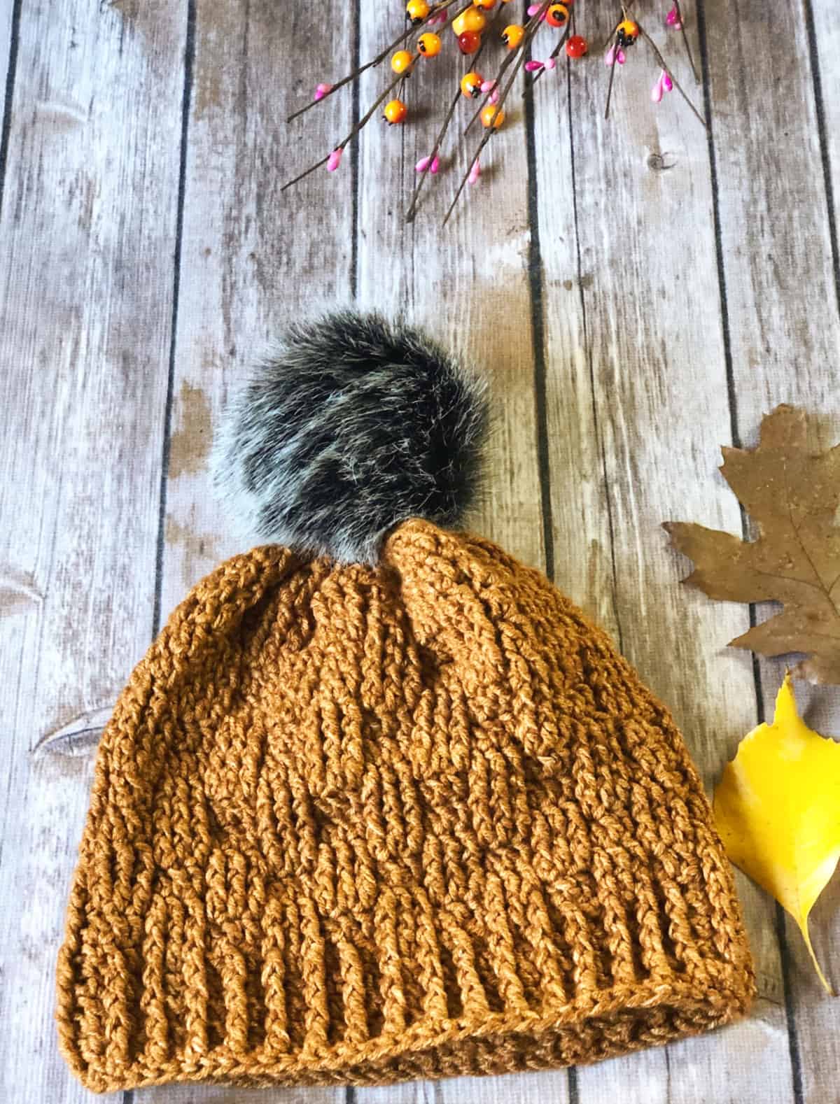 Textured basketweave crochet hat pattern with dark pom on woodback drop.