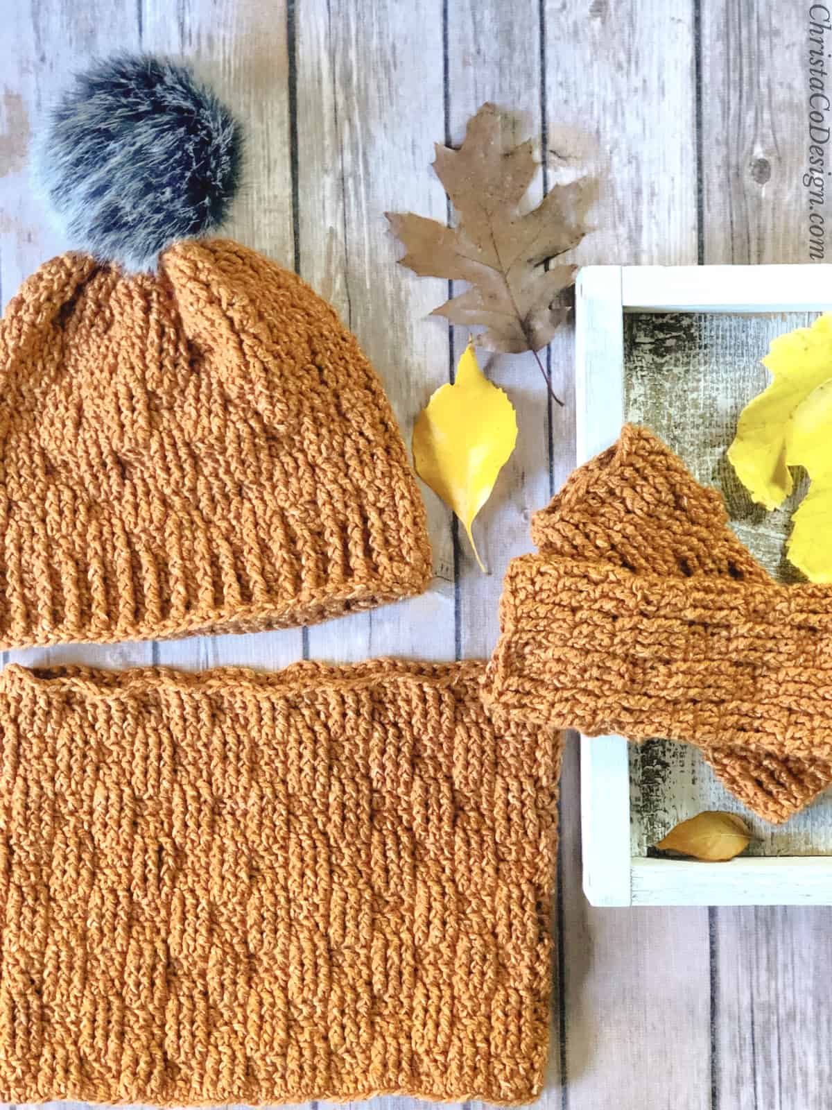 Crochet hat, fingerless gloves and cowl free crochet pattern in rust yarn on wood back ground.