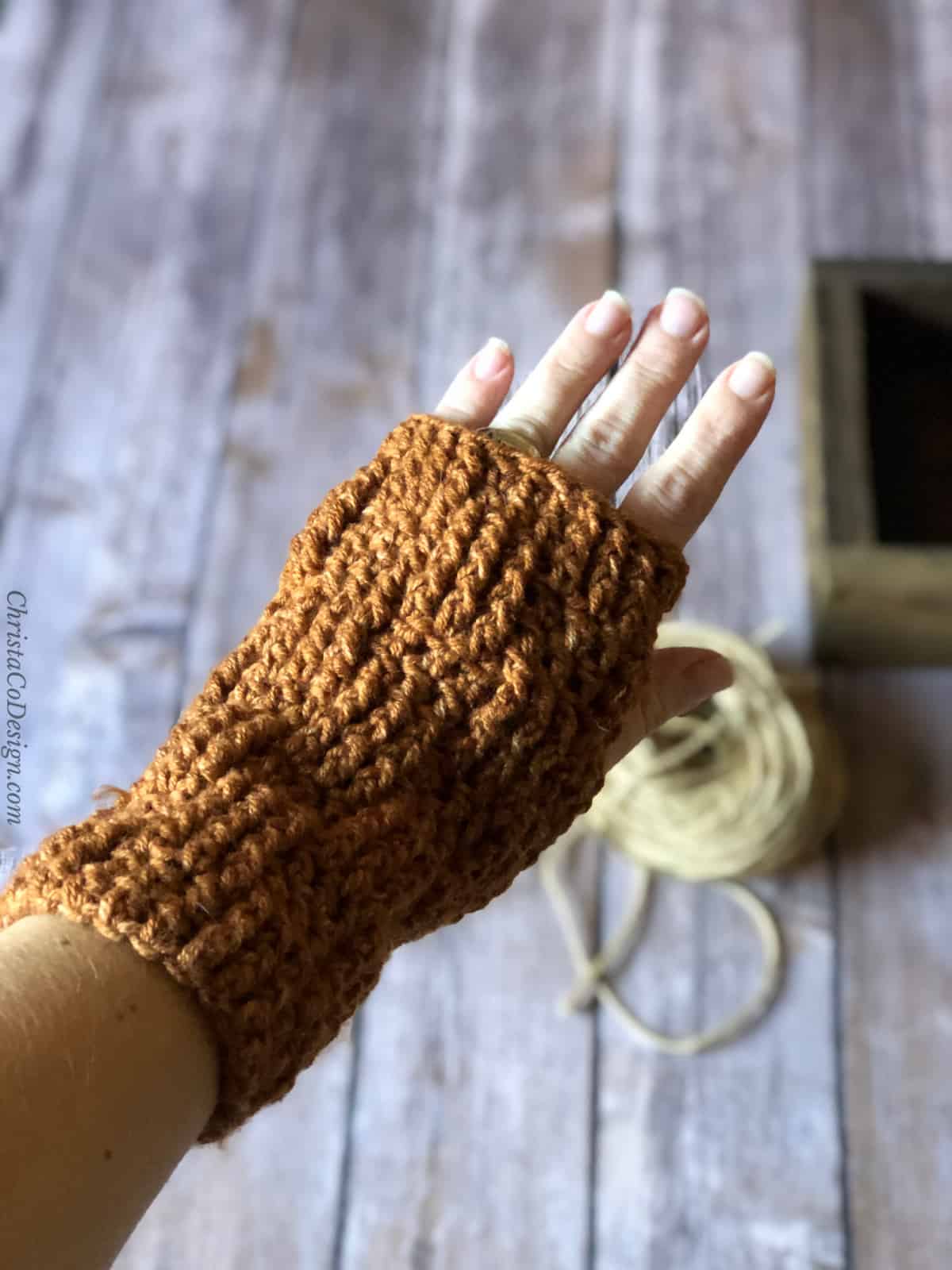 Woman's hand in crochet fingerless glove over wood backdrop.