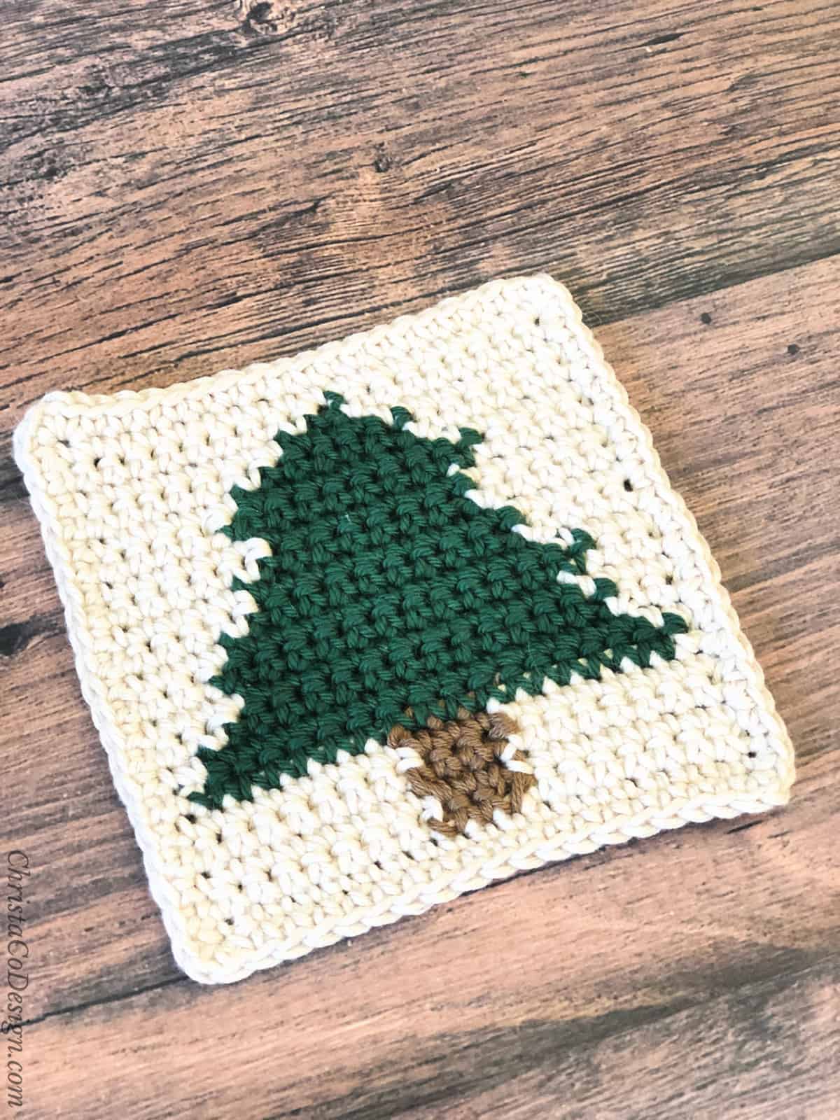 Crochet coaster in cream with dark green Christmas tree.